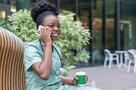 Young smiling african american woman in lab coat sitting on the bench and having coffeeの写真素材