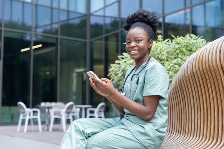 Pretty smiling female doctor with a phone in hand sitting on the benchの写真素材