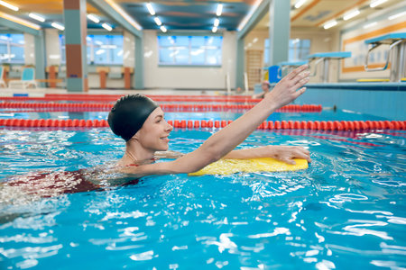Cute caucasian young woman swimming in the pool with a boardの写真素材