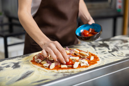 Cooker in apron working in the pizzeria kitchen and putting topping on the pizzaの写真素材