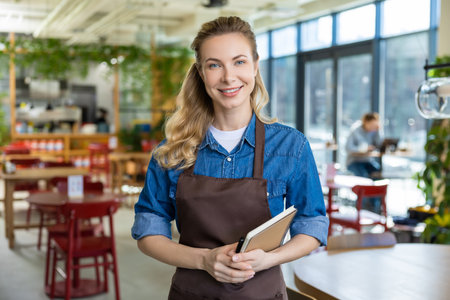 Pretty blonde woman in apron looking happy at her working place in pizzeriaの写真素材