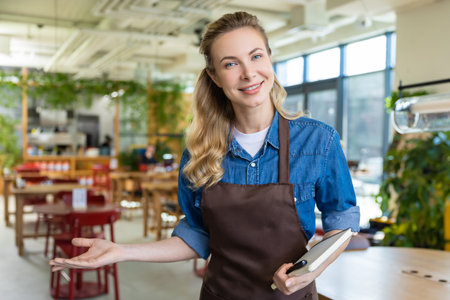 Pretty blonde woman in apron looking happy at her working place in pizzeriaの写真素材