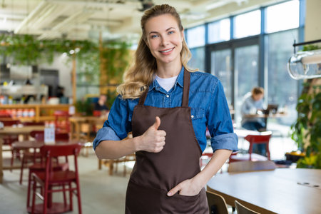 Pretty blonde woman in apron looking happy at her working place in pizzeriaの写真素材