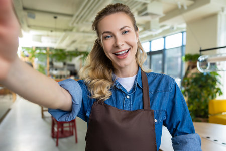 Cute blonde woman in apron making selfie and smilingの写真素材
