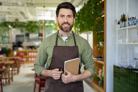 Young bearded man in apron looking confident while waiting for the client in pizzeriaの写真素材