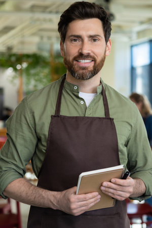 Young bearded man in apron looking confident while waiting for the client in pizzeriaの写真素材