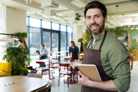 Young bearded man in apron looking confident while waiting for the client in pizzeriaの写真素材