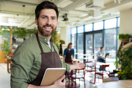 Young bearded man in apron looking confident while waiting for the client in pizzeriaの写真素材
