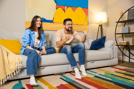 Man and woman in casual clothes watching match on TV at home cheering with excitementの写真素材