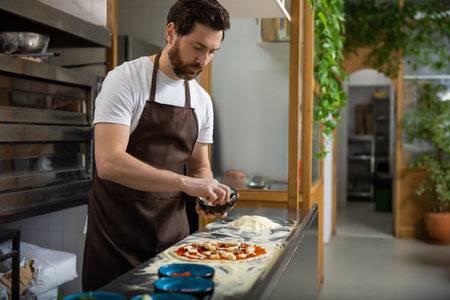 Man adds toppings pizza in kitchen arranging carefully creating foodの写真素材
