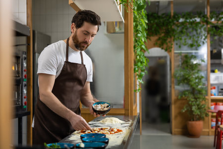 Man prepares pizza base in kitchen shaping dough carefully making mealの写真素材