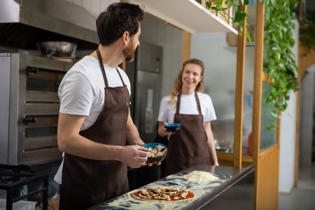 Man spreads sauce pizza in kitchen working smoothly preparing mealの写真素材