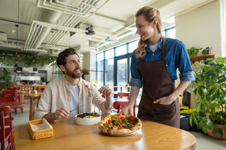 Waiter serving pizza to man at restaurantの写真素材