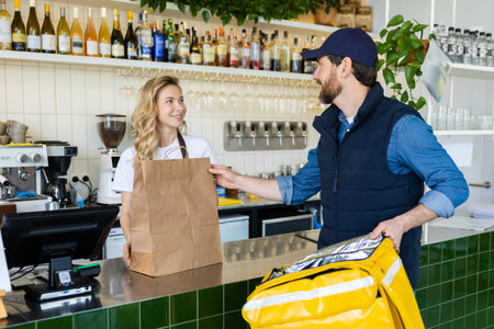 Cafe worker handing food order to courier at counter in modern cafe with paper bagの写真素材