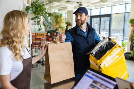 Cafe staff giving takeaway order to delivery courier at counter