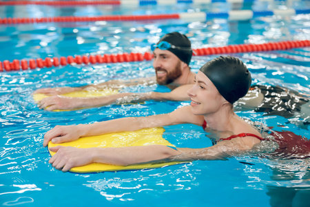 Young cute couple in swimming with boards in the poolの写真素材