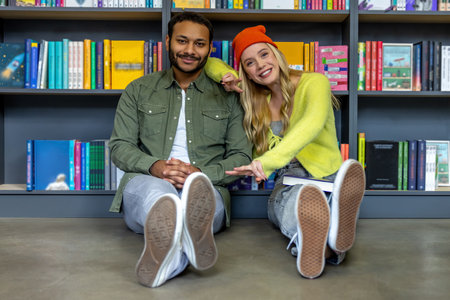 Multicultural man and woman sitting on floor in libraryの写真素材