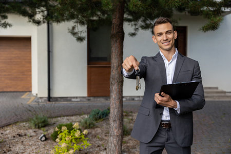 Real estate agent holding keys and clipboard in front of modern house for propertyの写真素材