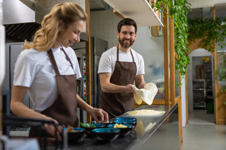 Woman smiling at man in kitchen preparing dough together enjoying baking timeの写真素材