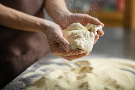 Person kneading dough in kitchen shaping pizza base carefully preparing mealの写真素材