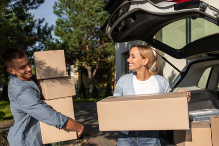 Young couple carrying boxes to the car while moving to a new house