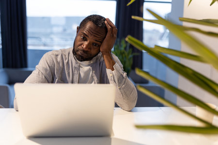 African american man at the laptop looking tired and suffering from a headacheの写真素材
