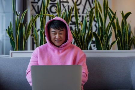 Asian young man in a pink hoodie at the laptop