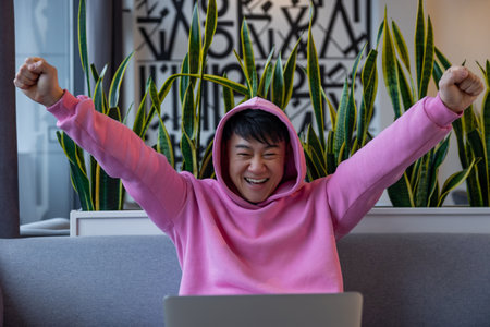 Asian young man in a pink hoodie at the laptop looking happyの写真素材