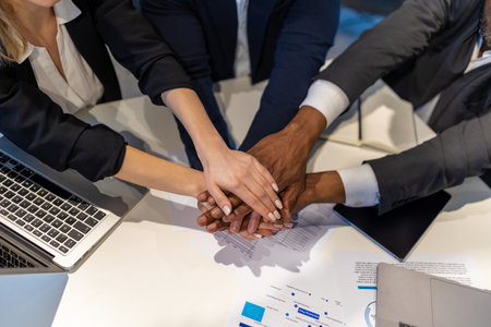 Professionals collaborating at meeting table uniting hands in positive gesture after project...