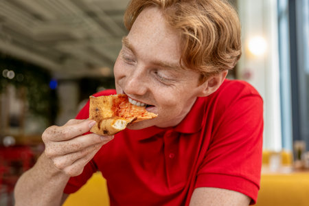 Young ginger man eating pizza and looking enjoyedの写真素材