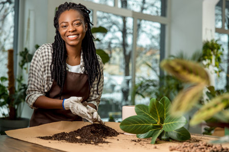Contented and enjoyed young woman planting flowers and looking busyの写真素材