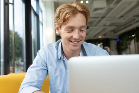 Young smiling man sitting at the table in a cafe and having a video call