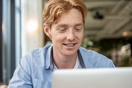 Young smiling man sitting at the table in a cafe and having a video call