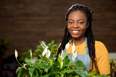 Cute smiling flower shop assistant with plants looking happyの写真素材