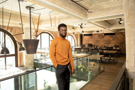 Confident young African man in glasses smiling and standing in modern office