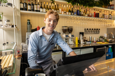 Barista using cash register smiling while working at modern coffee machine in bright cafÃ©