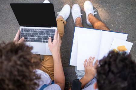 Teens sitting on the pavement in the park and studying together