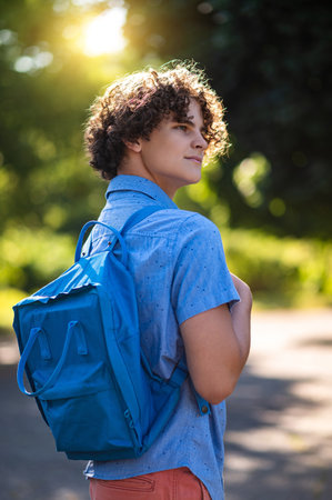 Curly-haired teen in blue tshirt spending time in the park