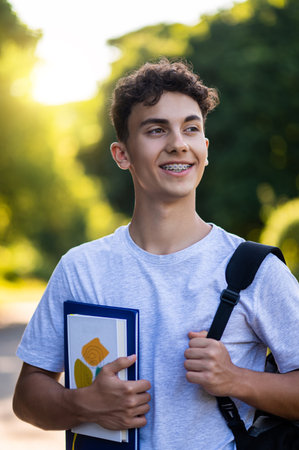 Handsome teen with backpack and books in hands looking joyfulの写真素材