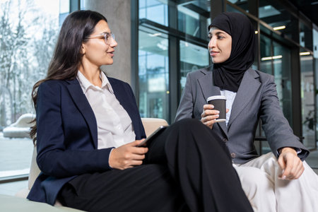 Two women sitting together, talking and looking involved and excitedの写真素材