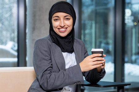 Woman in black hijab having a coffee break and looking contentedの写真素材