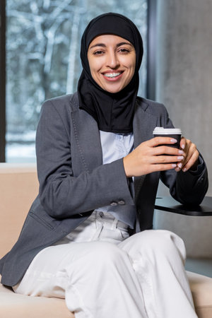 Woman in black hijab having a coffee break and looking contentedの写真素材