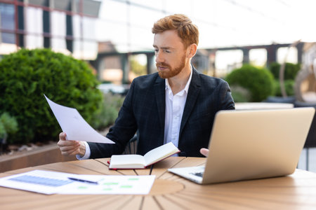 Young adult professional multitasking with computer and paperworkの写真素材