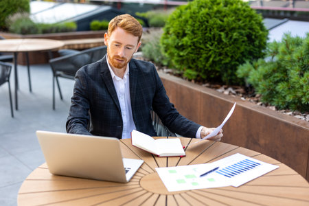 Caucasian businessman combining laptop work with paper filesの写真素材