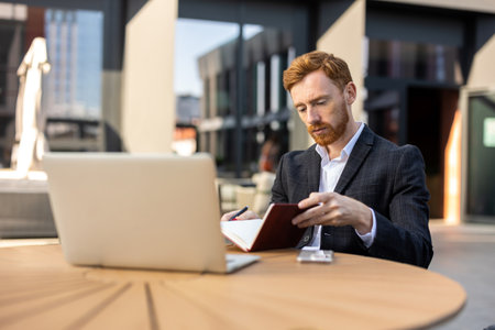 Businessman writing in paper planner at outdoor cafe tableの写真素材