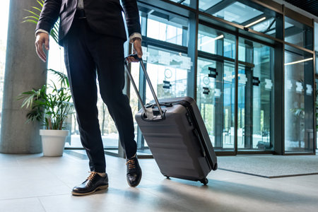 Close up of a man in formal wear carrying a suitcase while entering the business centerの写真素材