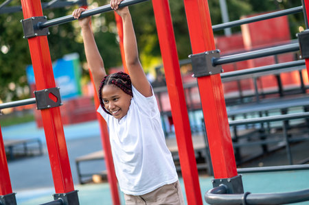 Happy cute girl hanging on the crossbar at the playground
