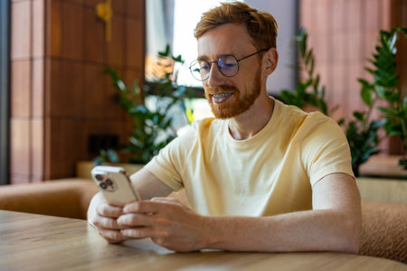 Ginger bearded man scrolling smartphone while sitting at cafe tableの写真素材