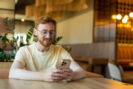 Bearded man focused on phone while seated indoors waiting his order in cafeの写真素材