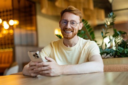Ginger-haired young adult scrolling mobile apps in cafeの写真素材